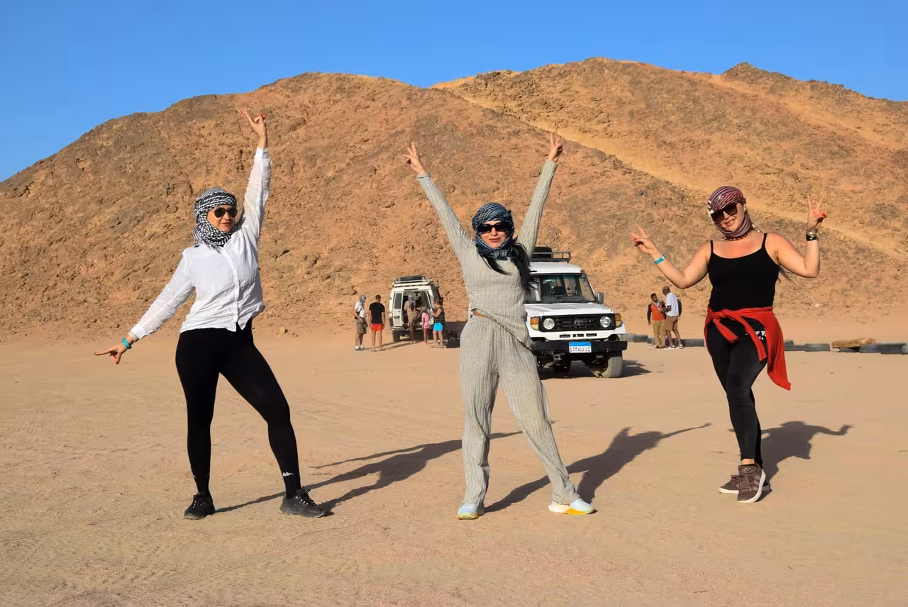Guests pose in Hurghada desert after ATV quad safari, with 4x4 support vehicles near Bedouin village