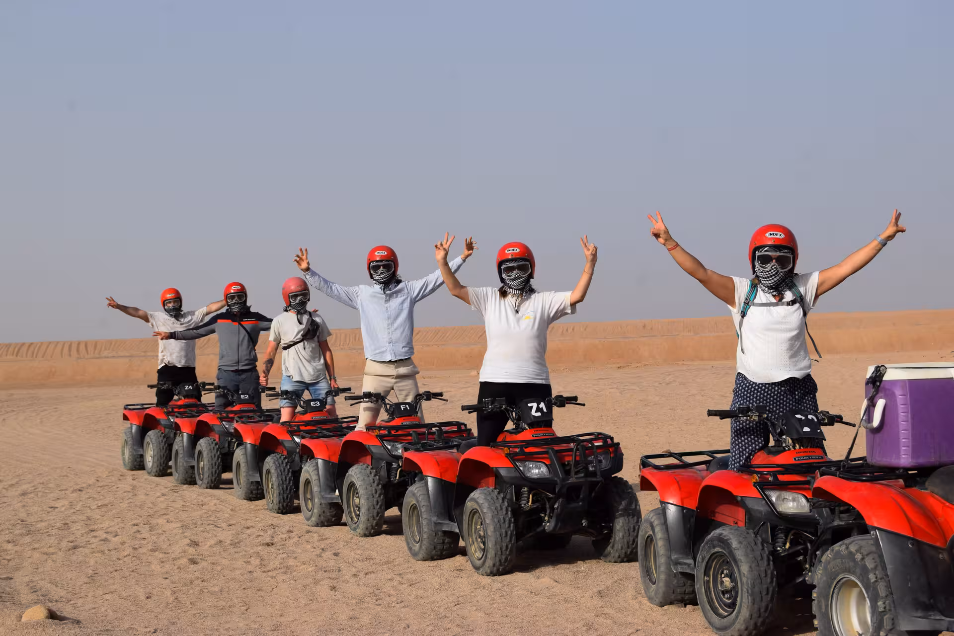Group on red ATVs in Hurghada desert, helmets on, ready for quad safari, camel ride and Bedouin village