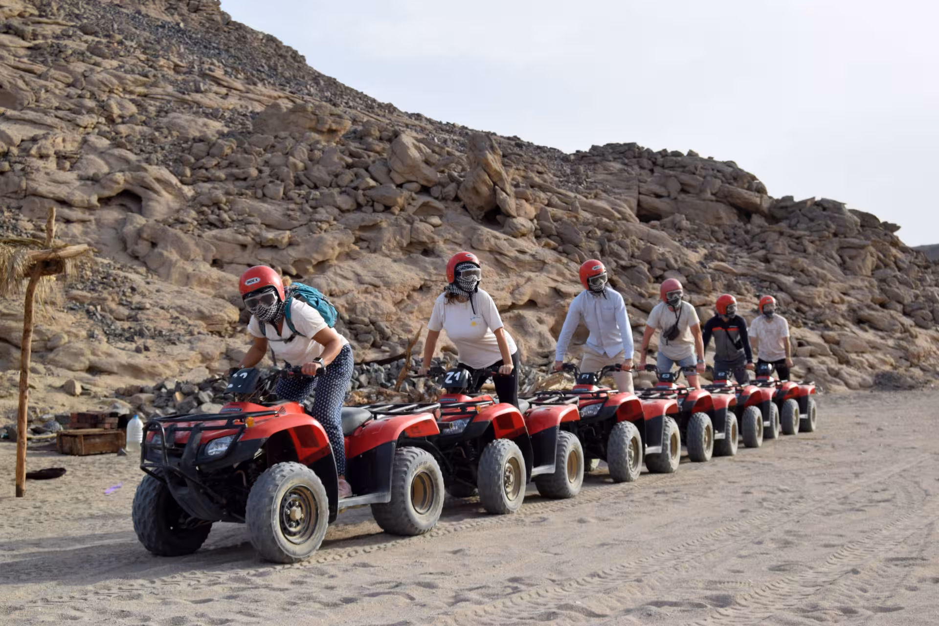 ATV quad convoy in Hurghada driving past rocky mountains on desert safari with Bedouin village and camel ride