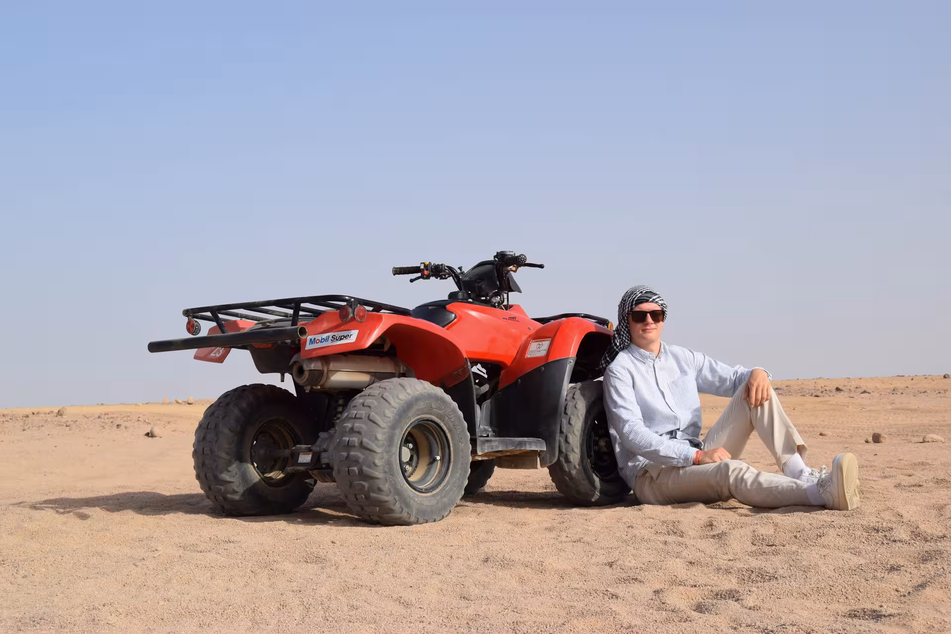 Traveler relaxing beside red ATV quad in Hurghada desert on quad safari and Bedouin village tour