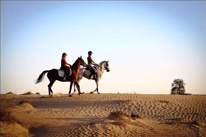 Two riders on horseback crossing Hurghada desert dunes, part of one-hour beach horse riding tour with transfer