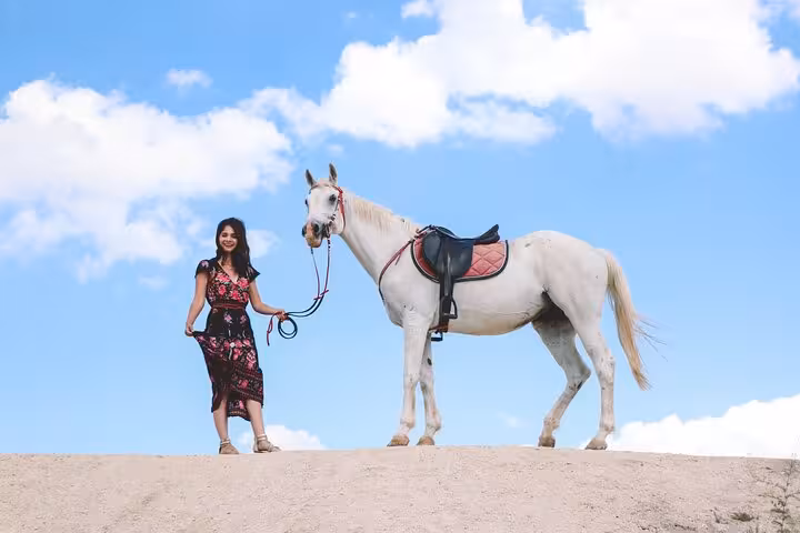Guest leading a white horse on Hurghada beach dunes under blue sky, one-hour horse riding tour with transfer