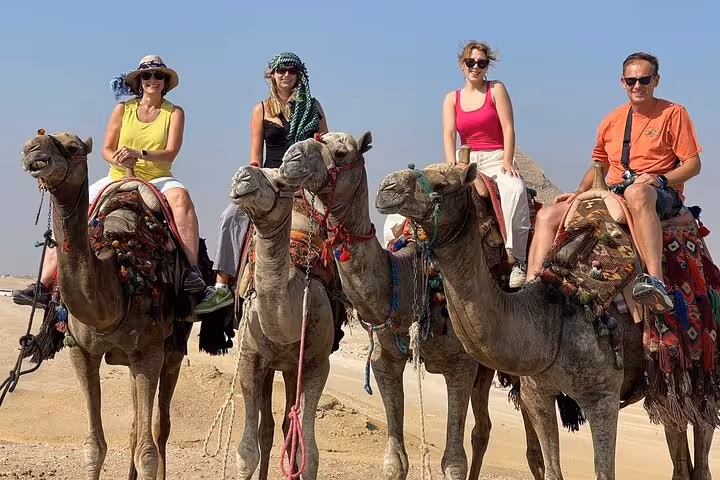 Tourists riding camels near the Giza Pyramids on Hurghada legacy trip to Cairo, iconic desert safari experience