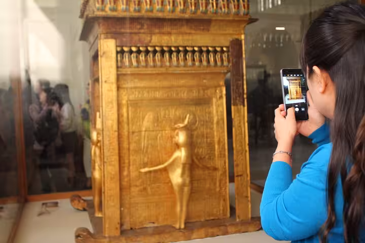 Traveler photographing a gilded ancient Egyptian artifact inside Cairo’s Grand Egyptian Museum on Hurghada day trip