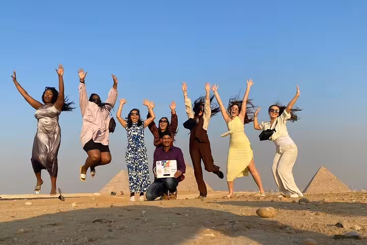 Happy travelers jumping with Giza Pyramids in background during Hurghada to Cairo legacy trip and Grand Museum tour