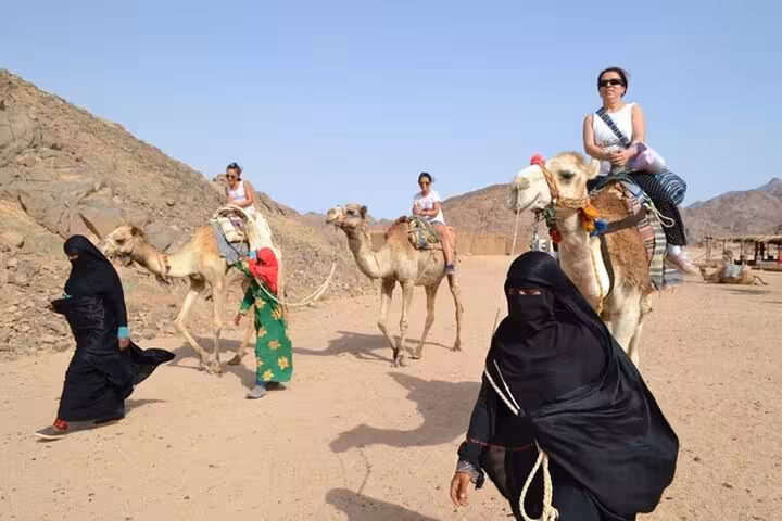 Tourists riding camels in Hurghada desert on a Jeep Super Safari to a Bedouin village with dinner show
