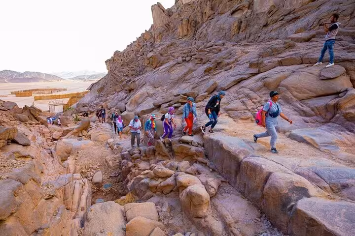 Group hiking rocky canyon on Hurghada Jeep Super Safari adventure to Bedouin village, dinner and live show