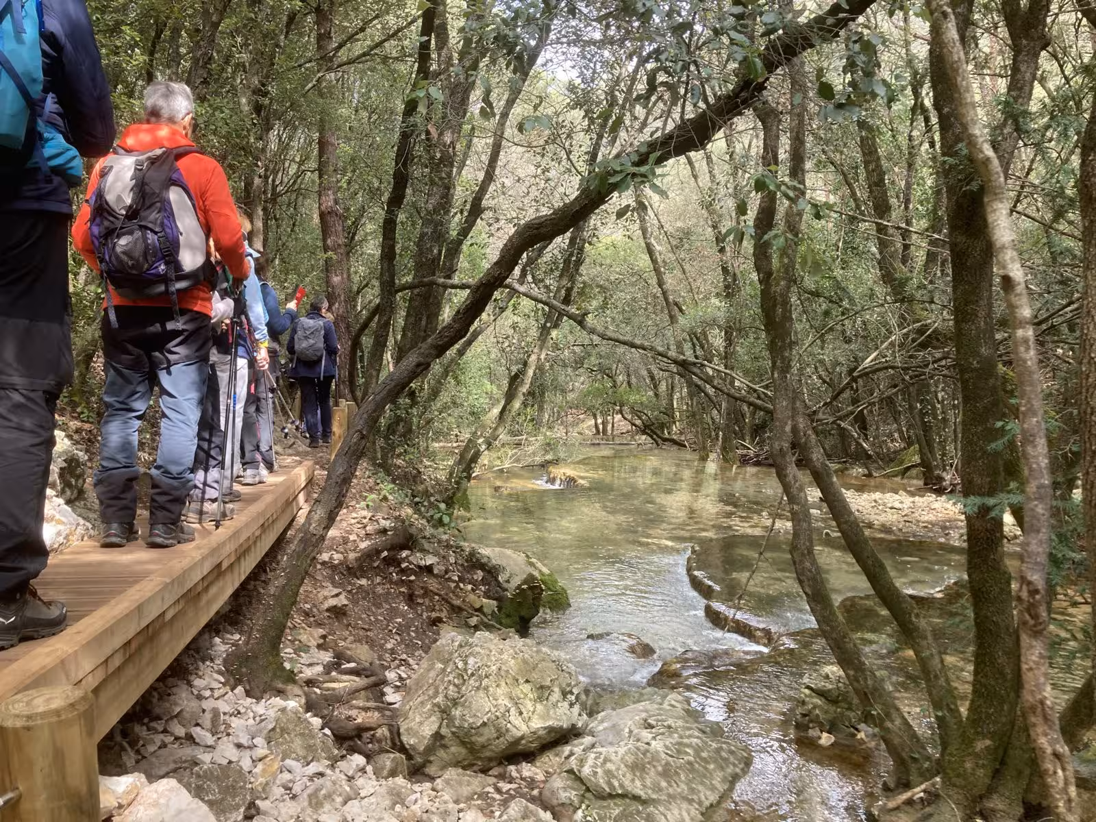 Hikers on a wooden boardwalk beside the Huveaune River, scenic nature trail to the river source in Provence