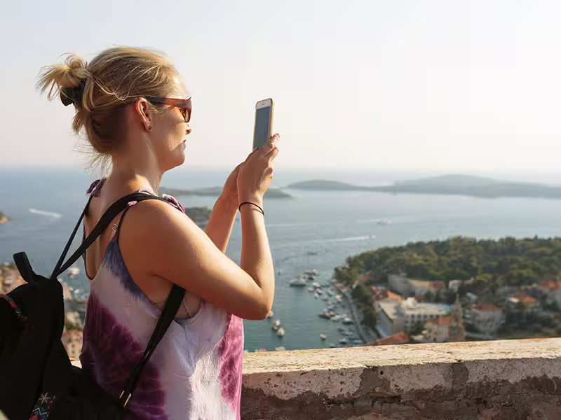 Traveler photographing panoramic Hvar Town harbor and Pakleni Islands, highlight of a private boat tour