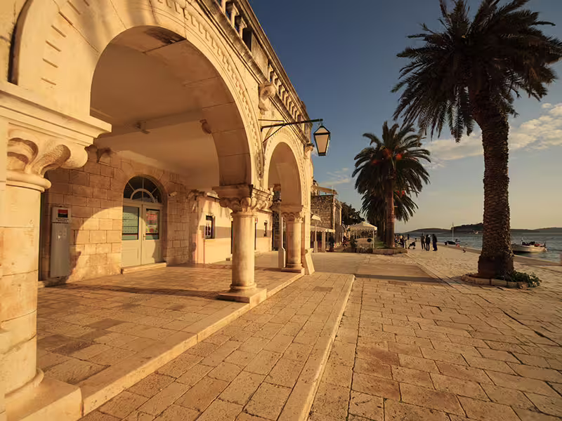 Sunlit waterfront promenade with stone arches and palm trees, a scenic stop on a private Hvar Brac Solta boat tour
