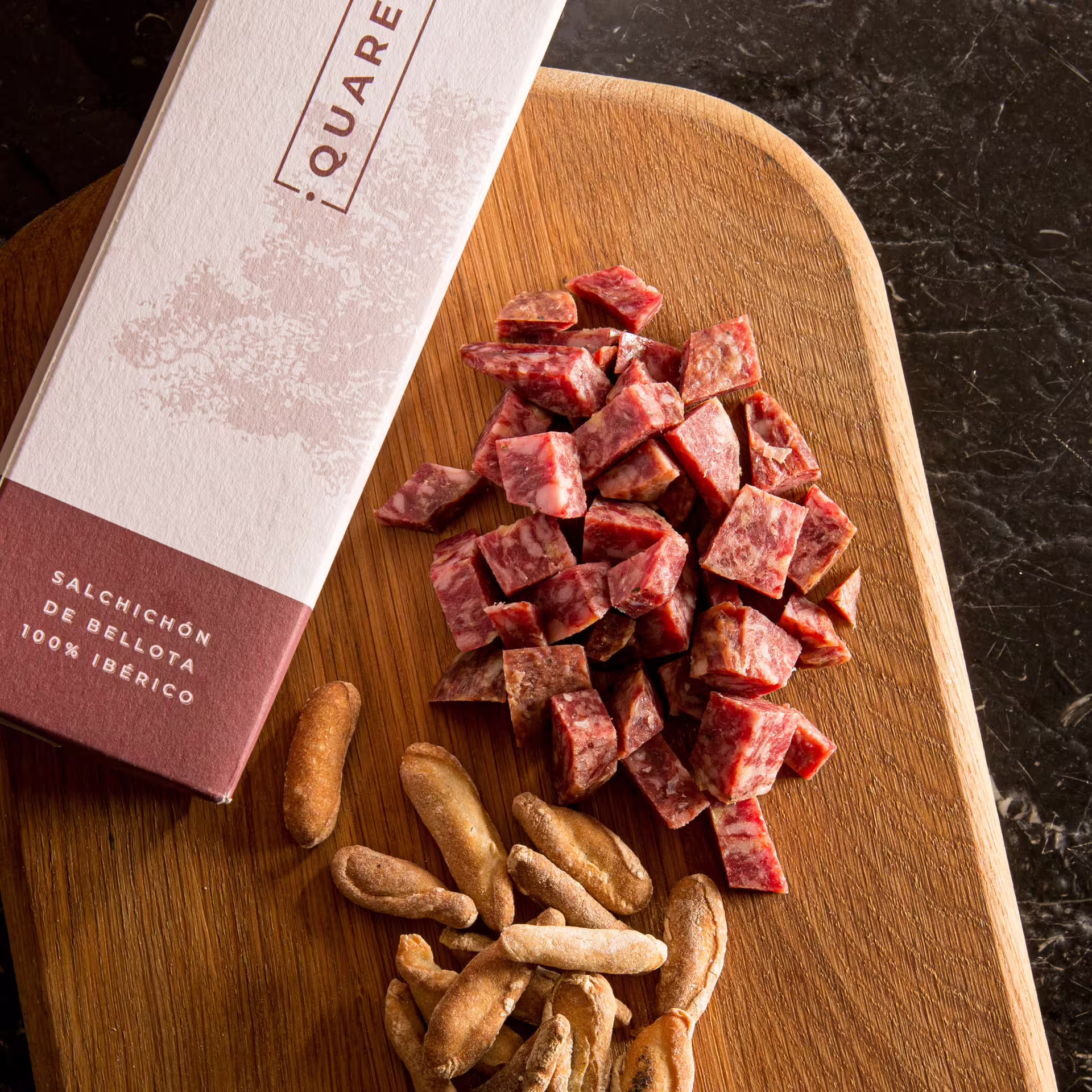 Sliced Iberian salchichón and breadsticks on a wooden board, showcasing authentic flavors of a Seville private food tour.