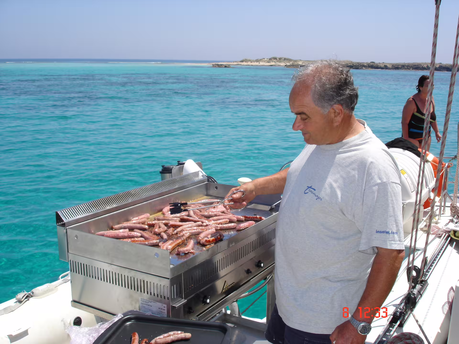 Onboard barbecue cooking sausages on Ibiza to Formentera Illetas catamaran cruise with meal included
