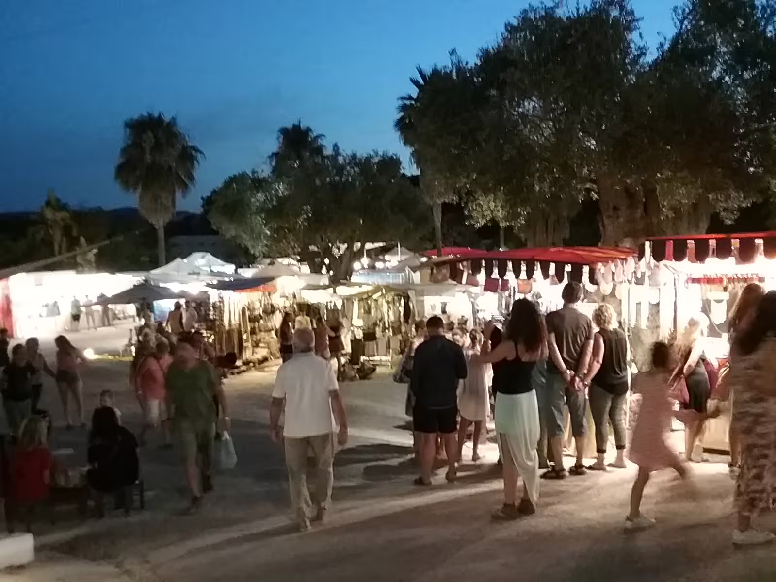 Evening crowd at Las Dalias hippie market Ibiza on sunset bus tour, browsing lit artisan stalls