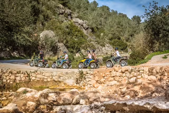 Grupo en quad tour por Ibiza cruzando un camino rural junto a arroyo, naturaleza y aventura medio día