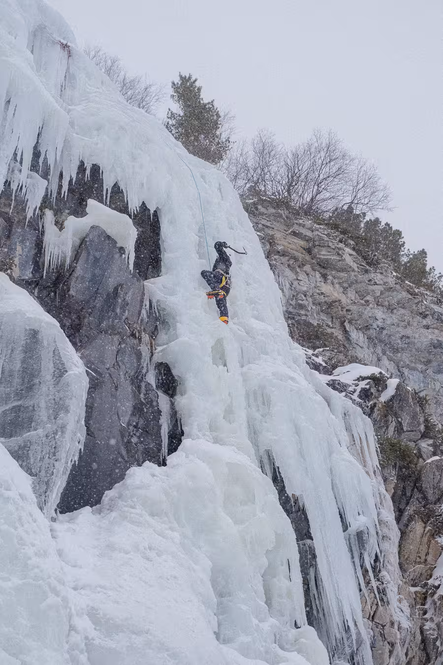 Ice climber ascending a rugged ice wall on a thrilling Rovaniemi adventure amidst snowy conditions.
