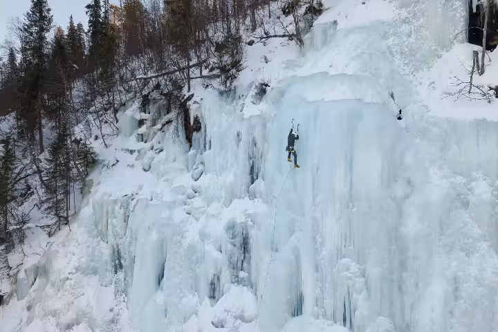 Climber tackling a vast frozen cliff in a serene forest setting on an ice climbing tour from Rovaniemi.