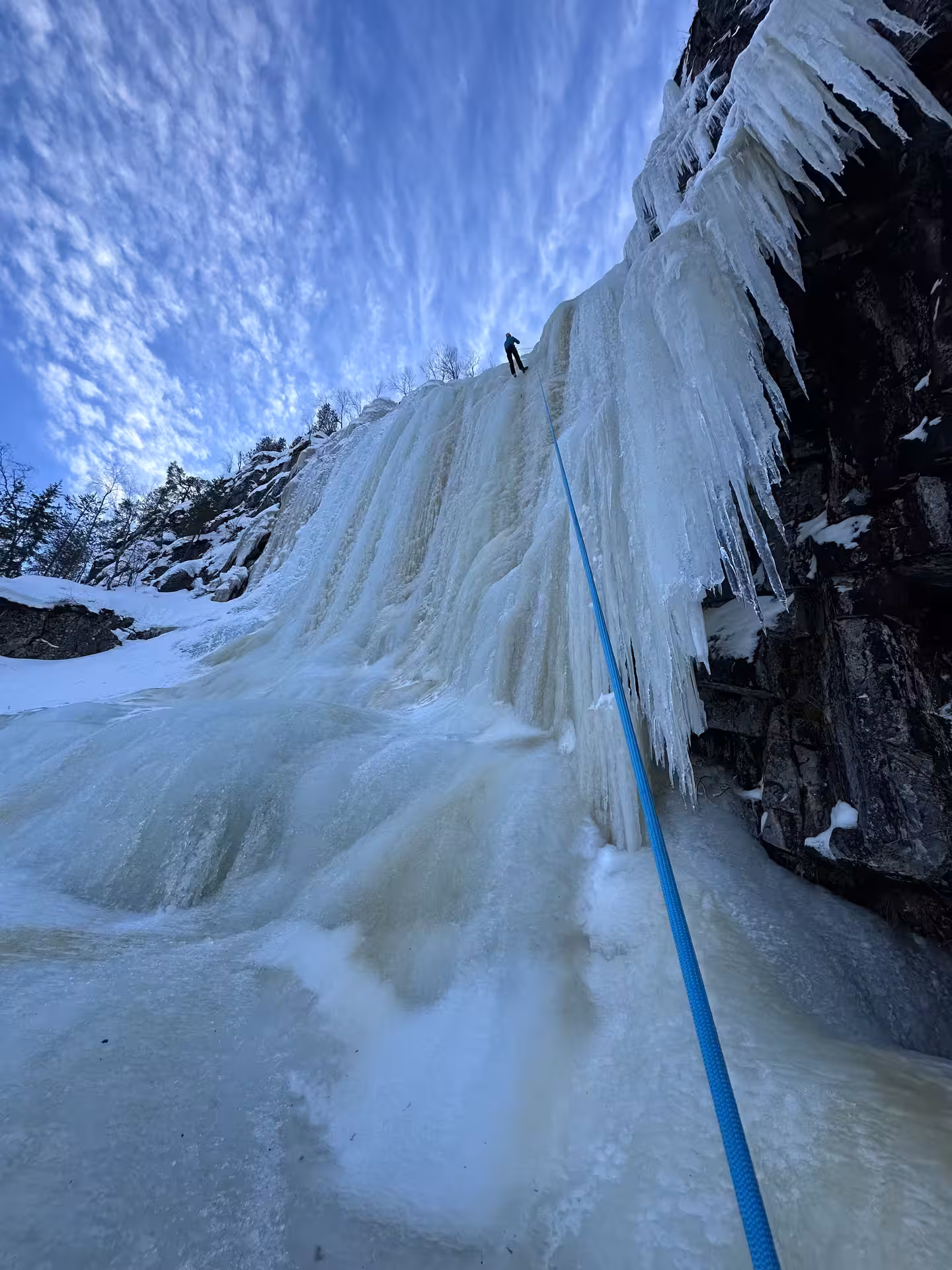 Adventurer scaling a frozen waterfall under a vibrant sky during an ice climbing tour from Rovaniemi.