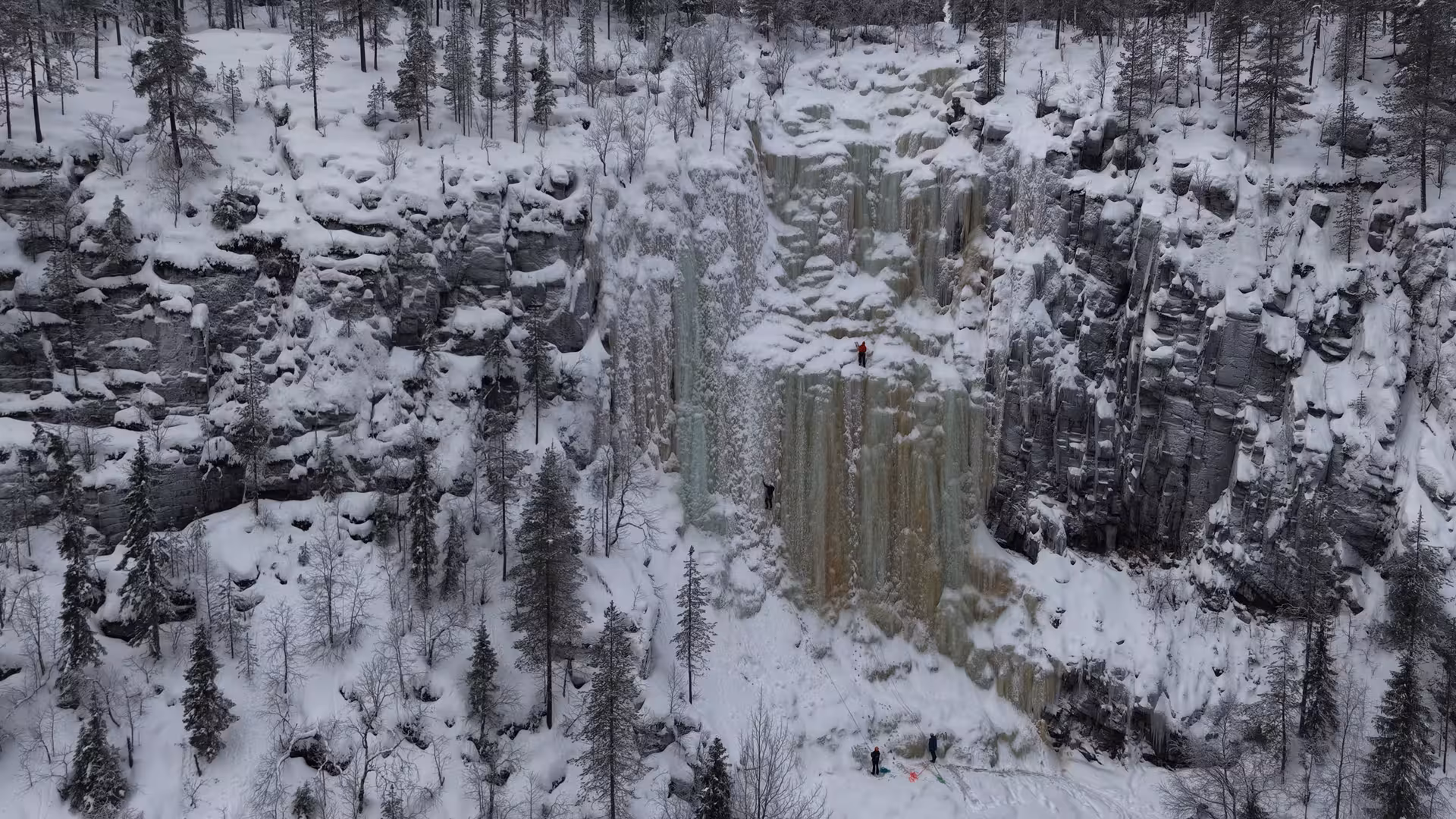 Adventurers ice climbing on a frozen waterfall in snowy Rovaniemi, surrounded by a scenic winter forest.