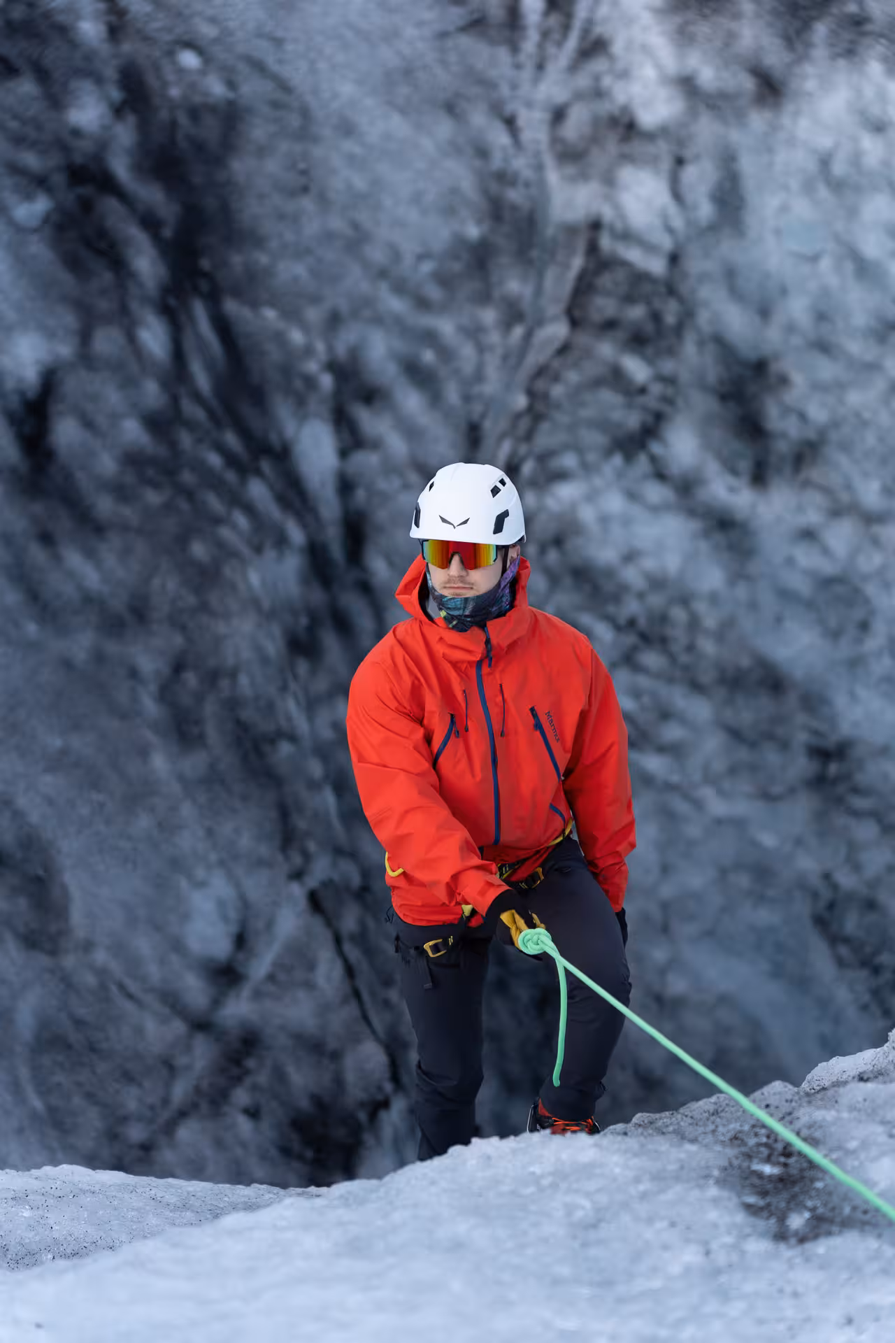 Climber in helmet and crampons belays on Sólheimajökull glacier during guided ice climbing tour in Iceland