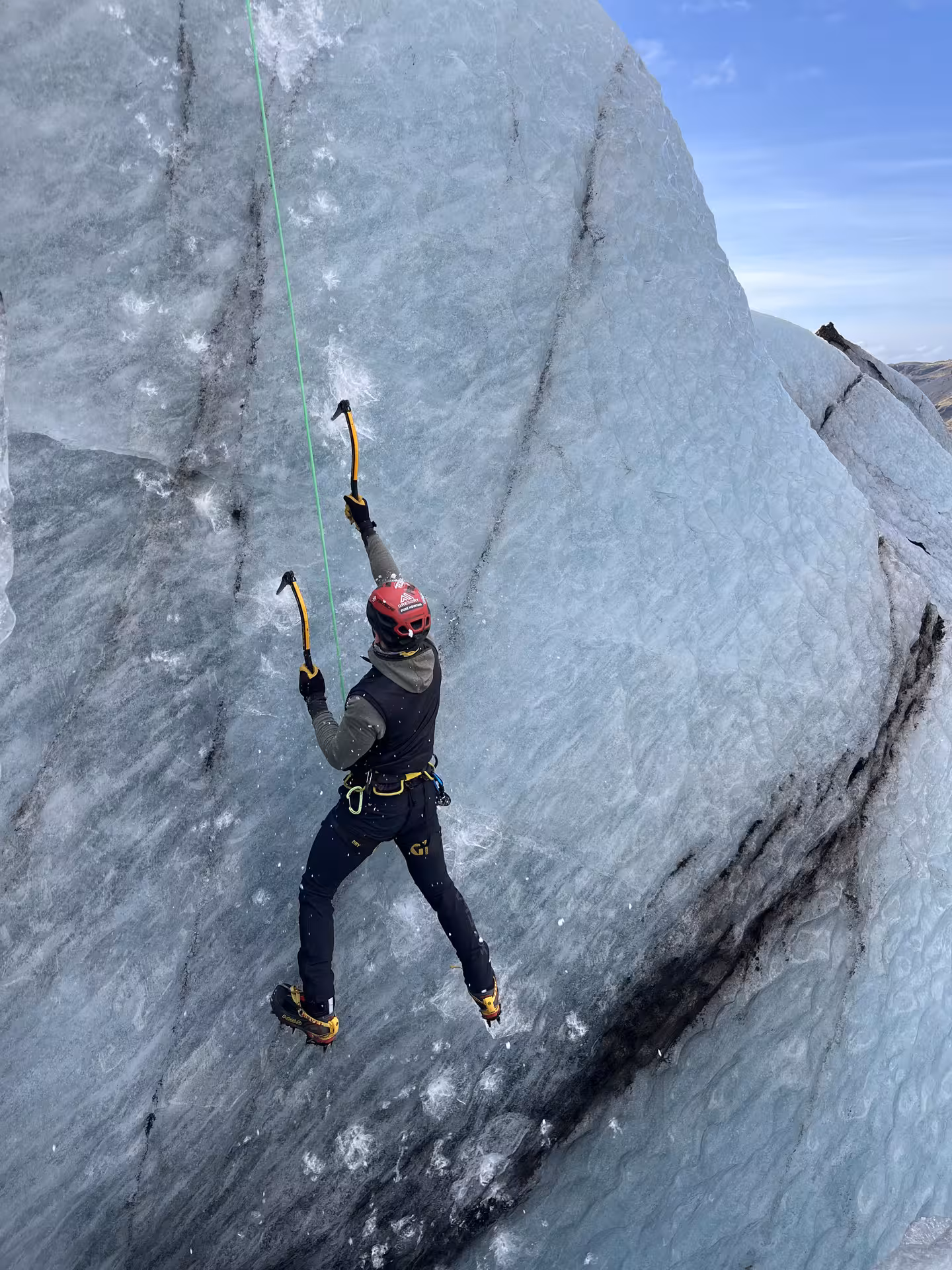 Roped climber ice climbing Sólheimajökull glacier wall in Iceland with ice axes and crampons