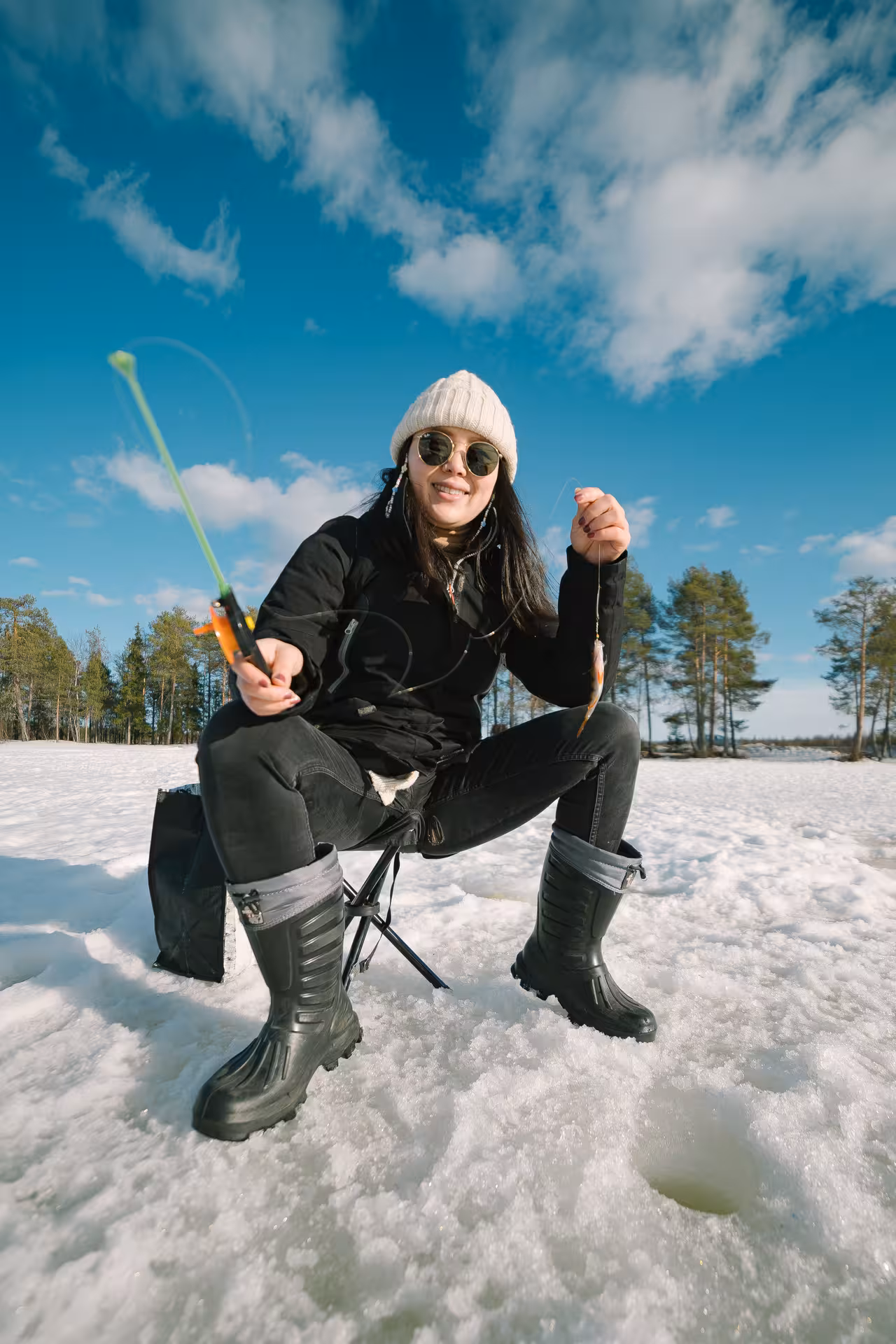 Smiling ice fisherwoman holds a catch on a sunny day, showcasing local ice fishing adventure.