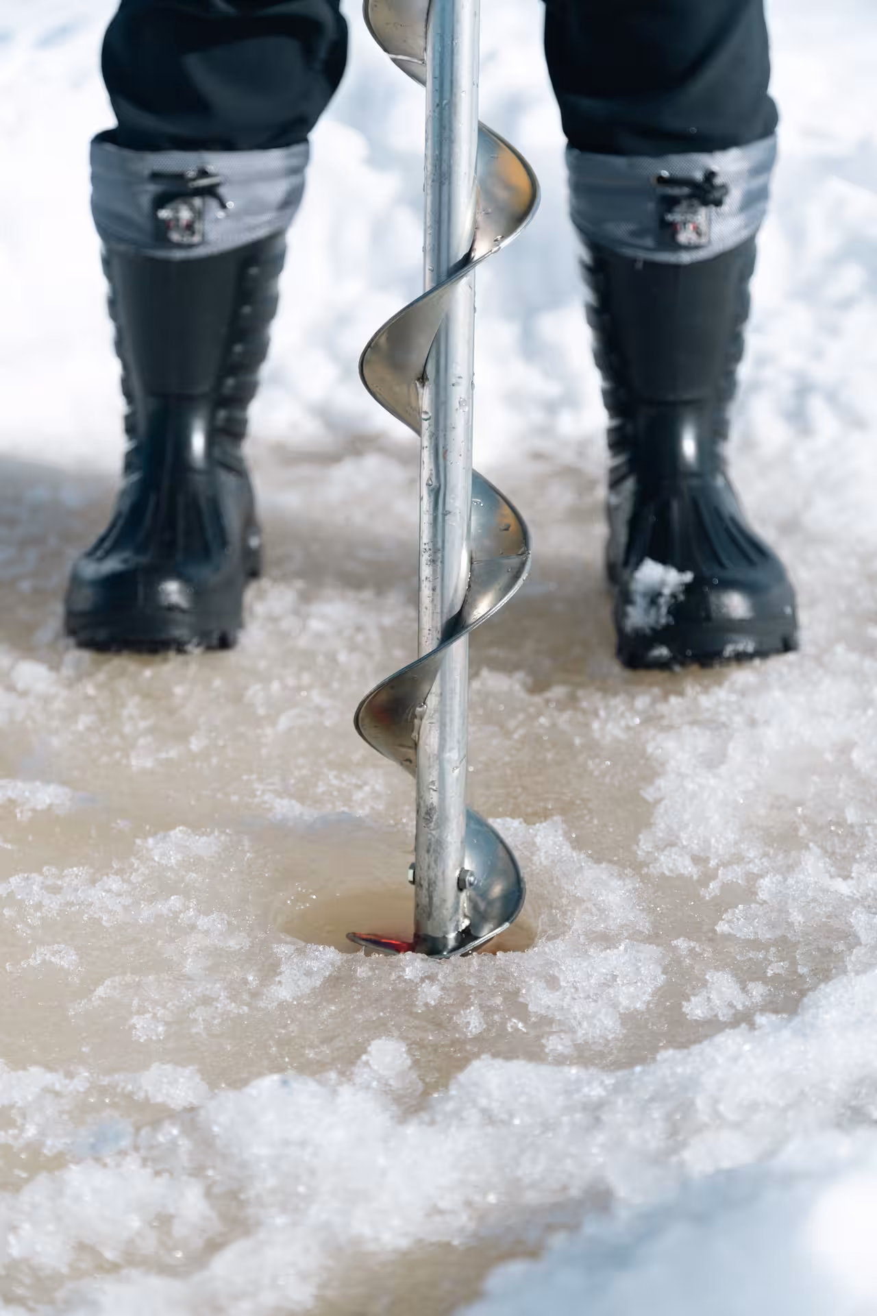 Close-up of auger drilling ice, essential tool for ice fishing adventures on frozen lakes.