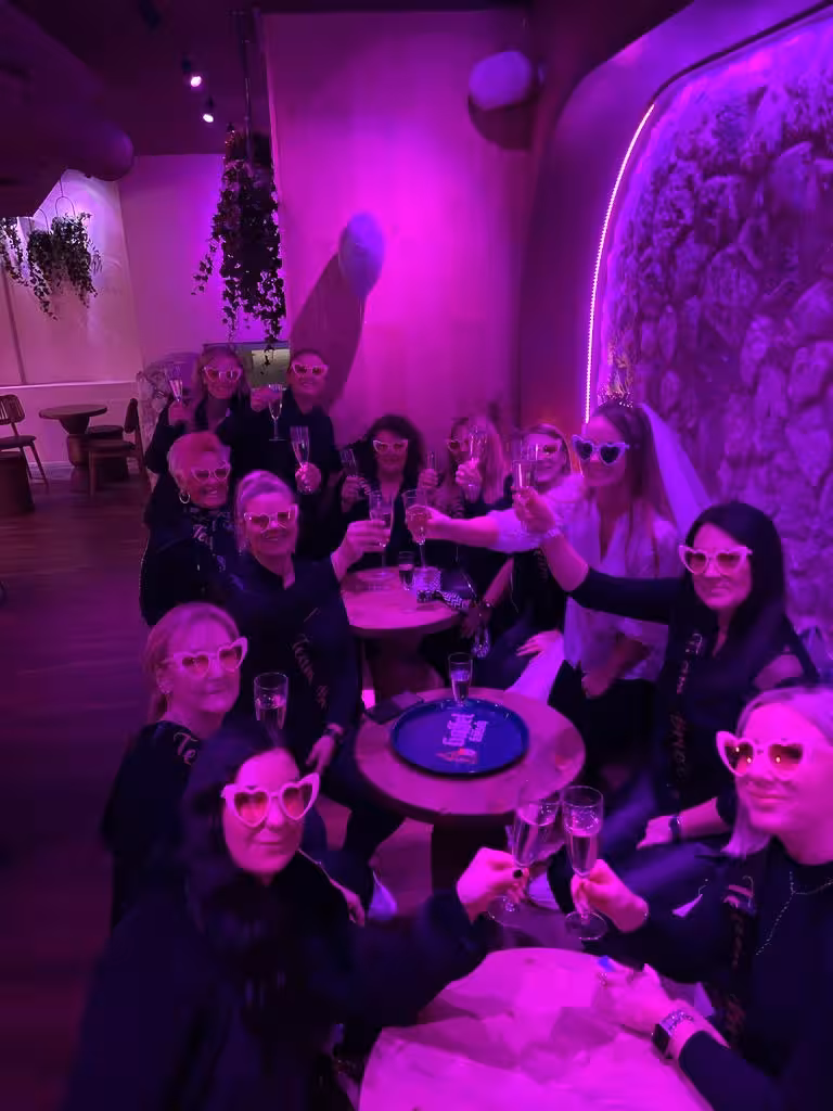 Group celebrating at IceBar Cologne, enjoying drinks with vibrant purple lighting and heart-shaped glasses.