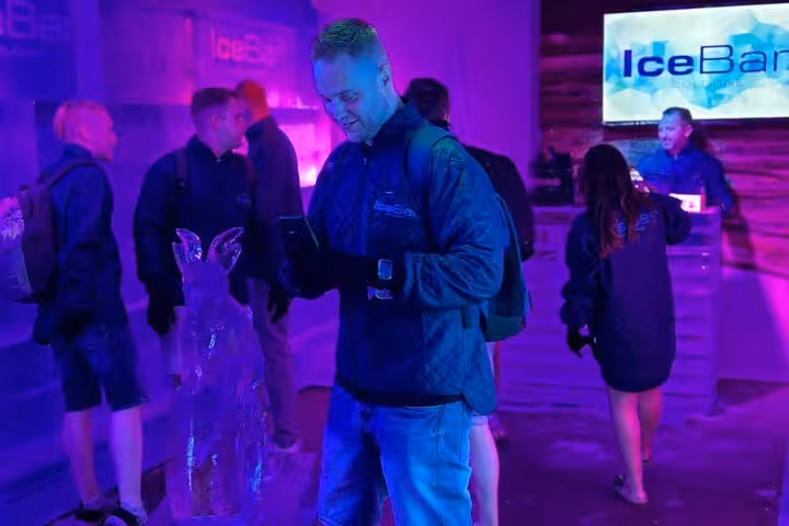 Visitors enjoy a vibrant, neon-lit atmosphere inside the IceBar Cologne, surrounded by intricate ice sculptures.