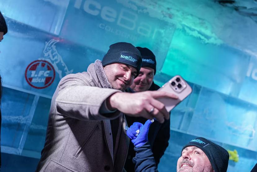 Visitors taking a selfie at IceBar Cologne, wearing branded hats and surrounded by icy decor and logos.