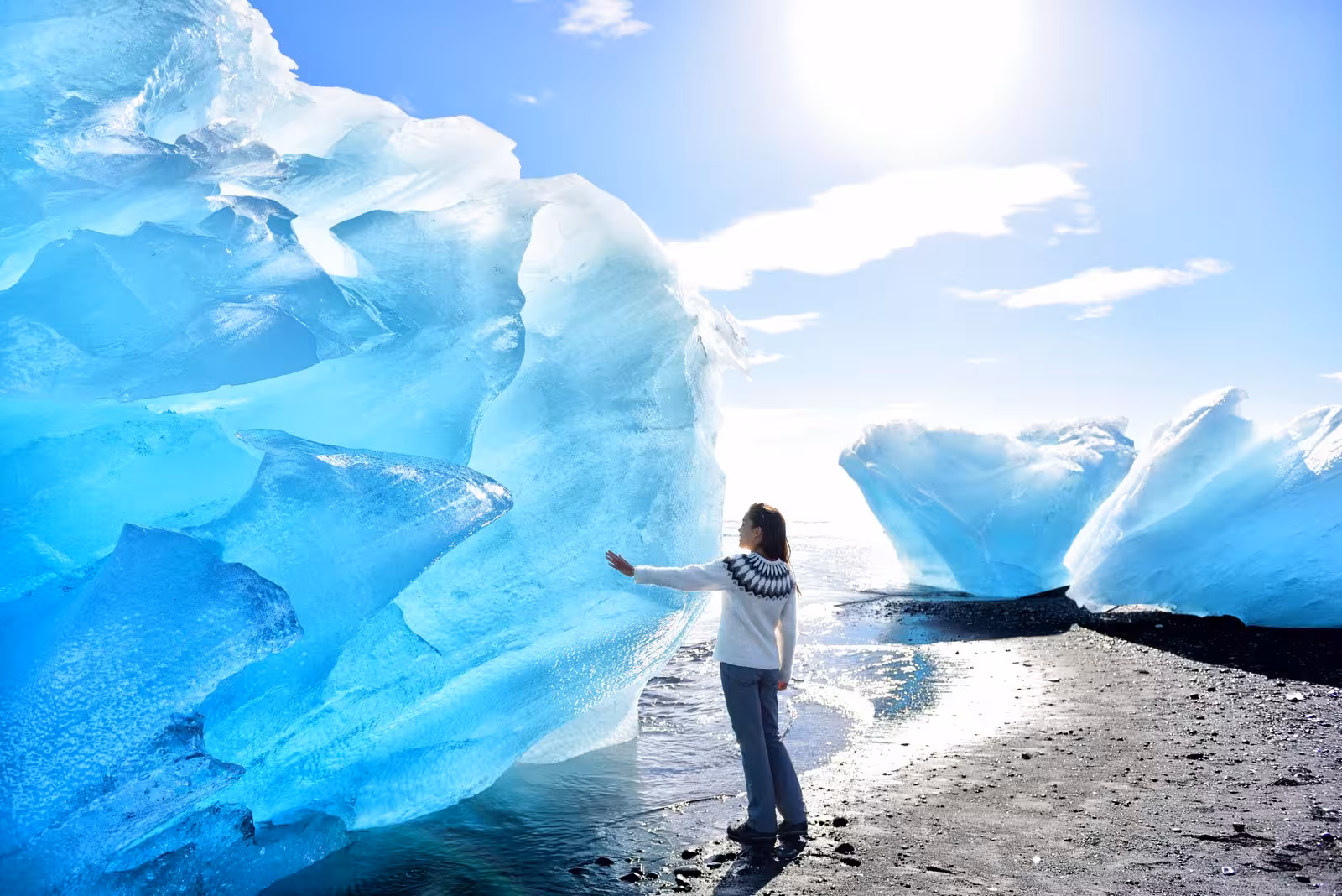 Visitor touches blue iceberg on Diamond Beach near Jökulsárlón, must-see stop on 7-day small group Iceland trip
