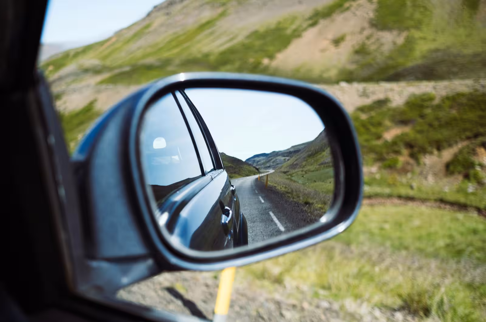 Reflection of a scenic Icelandic road in a car mirror on the Beautiful South self-drive adventure.