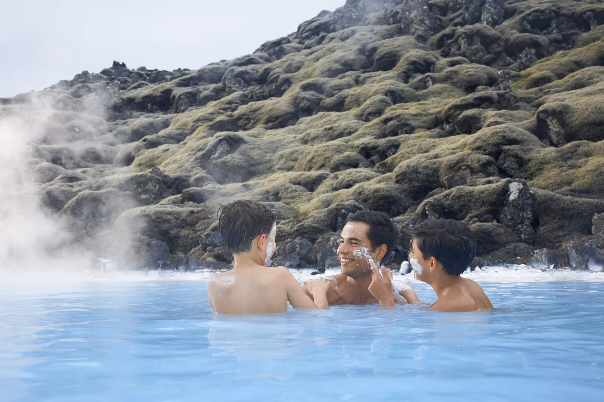 Family enjoying the geothermal waters of Iceland's Blue Lagoon with scenic moss-covered rocks.