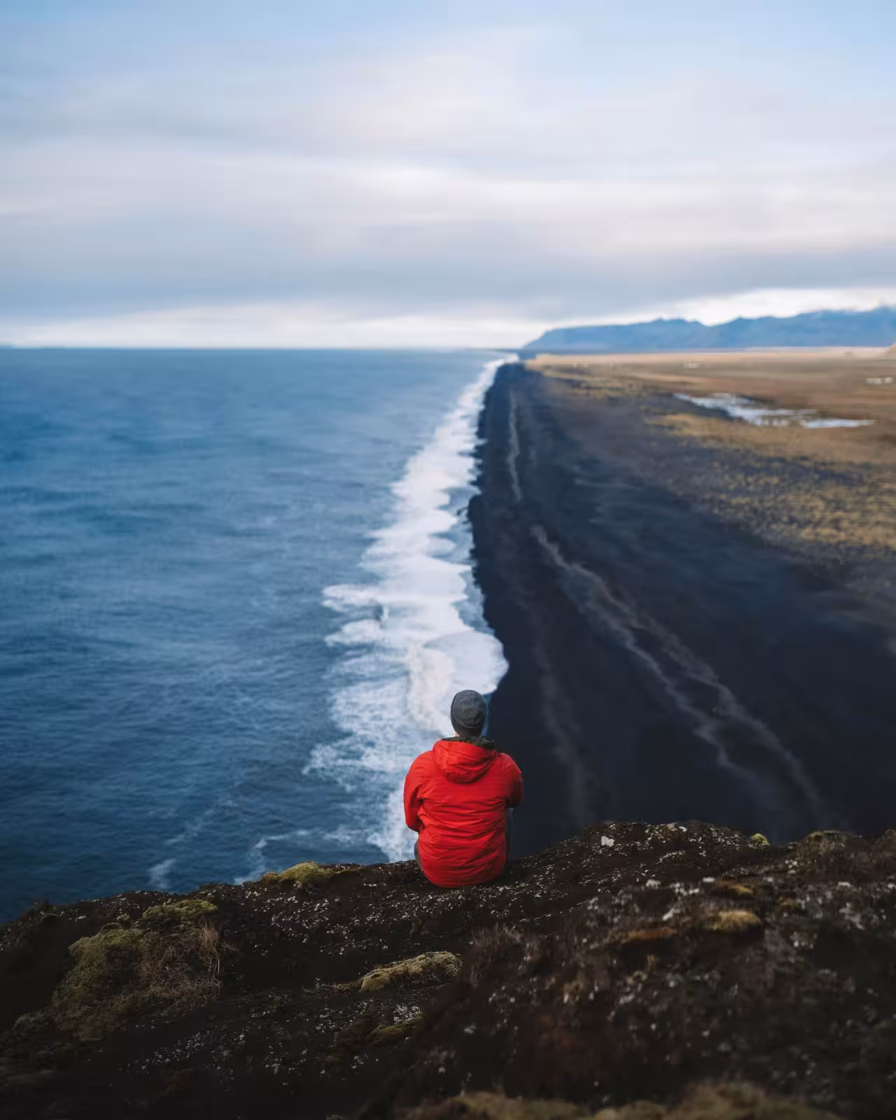 Person admiring the dramatic view of Iceland’s black sand coastline from a clifftop vantage point.