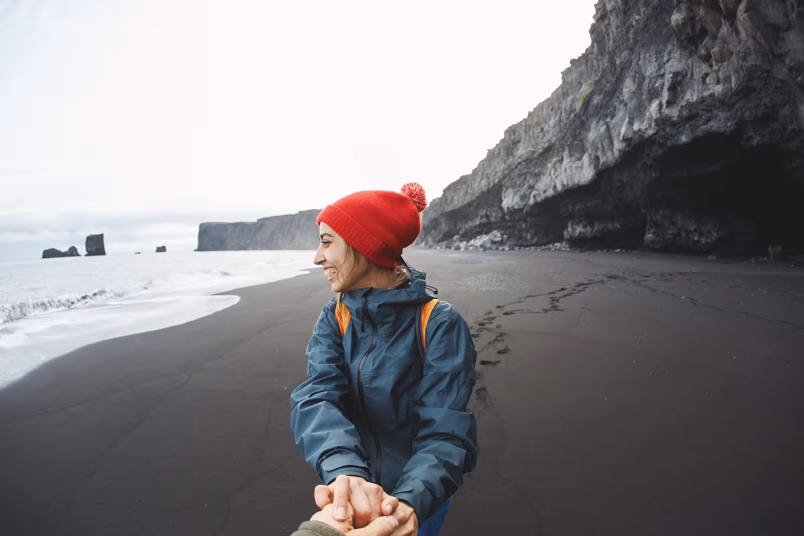 Woman in red beanie explores Iceland's iconic Reynisfjara black sand beach on a 6-day self-drive tour.