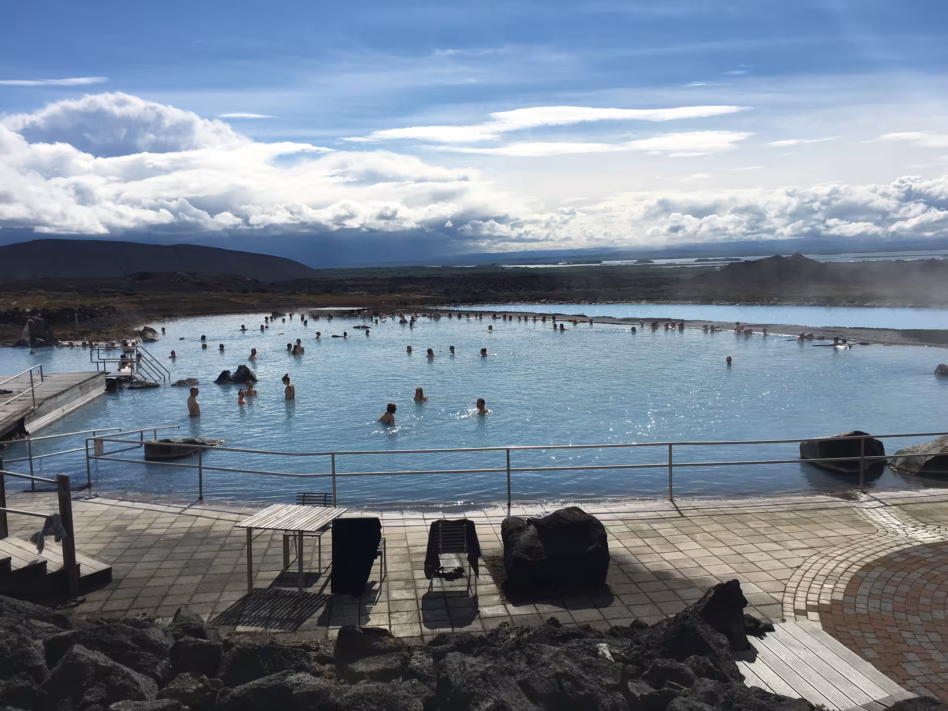 Relaxing geothermal hot spring with visitors enjoying the natural spa under a bright sky, ideal for a bespoke Iceland tour.