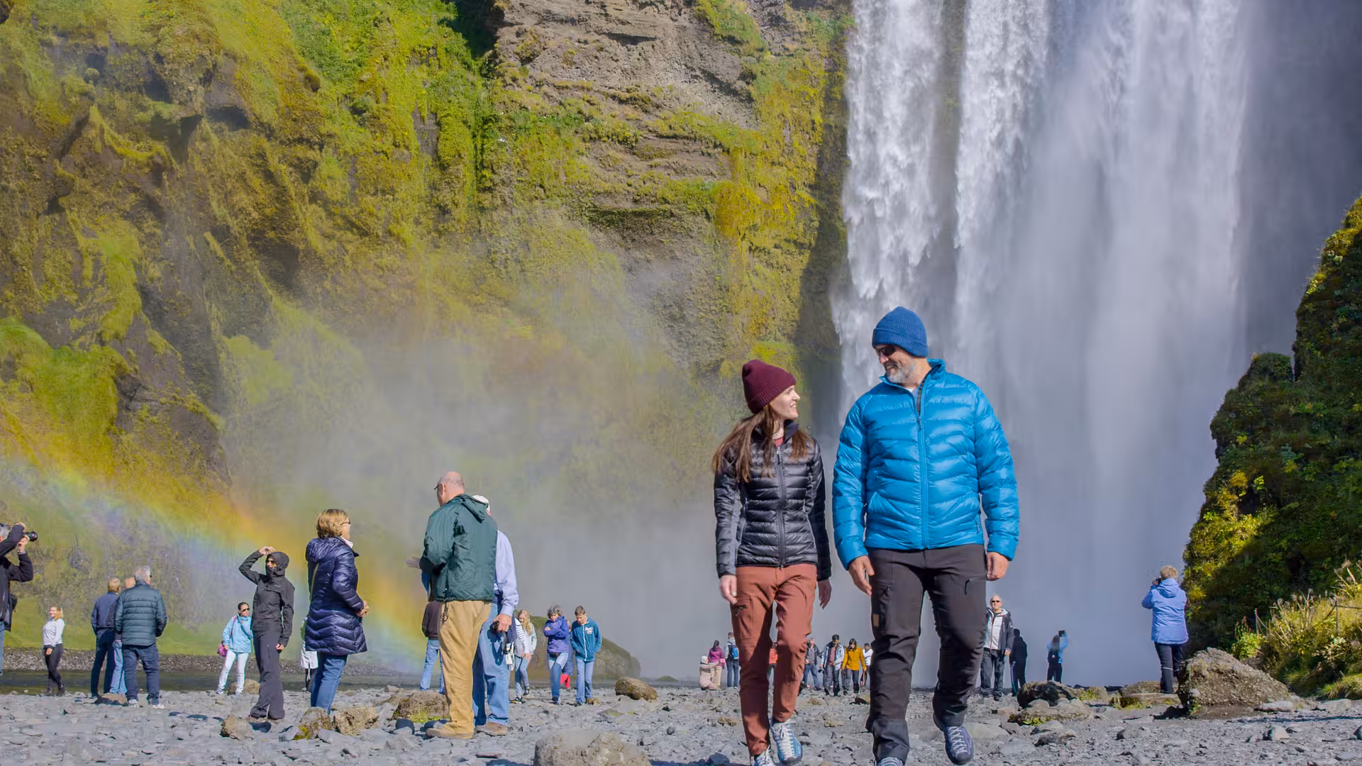 Tourists enjoy a vibrant rainbow at Skógafoss waterfall, a highlight of the Iceland Glacier Lagoon tour.