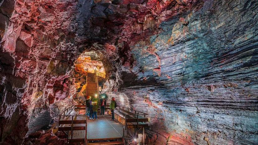 Tourists exploring colorful volcanic lava tunnel cave with metal walkways and stairs in Iceland