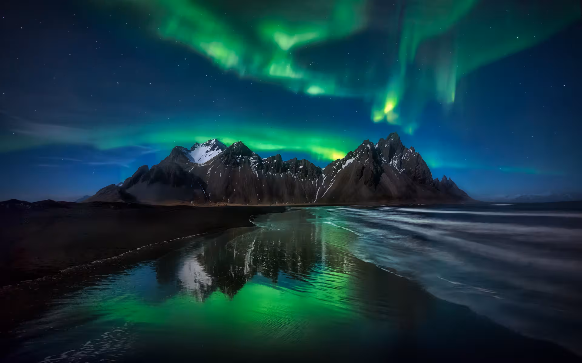 Majestic Northern Lights illuminate snow-capped mountains and serene lagoon on Iceland's 5-day tour.