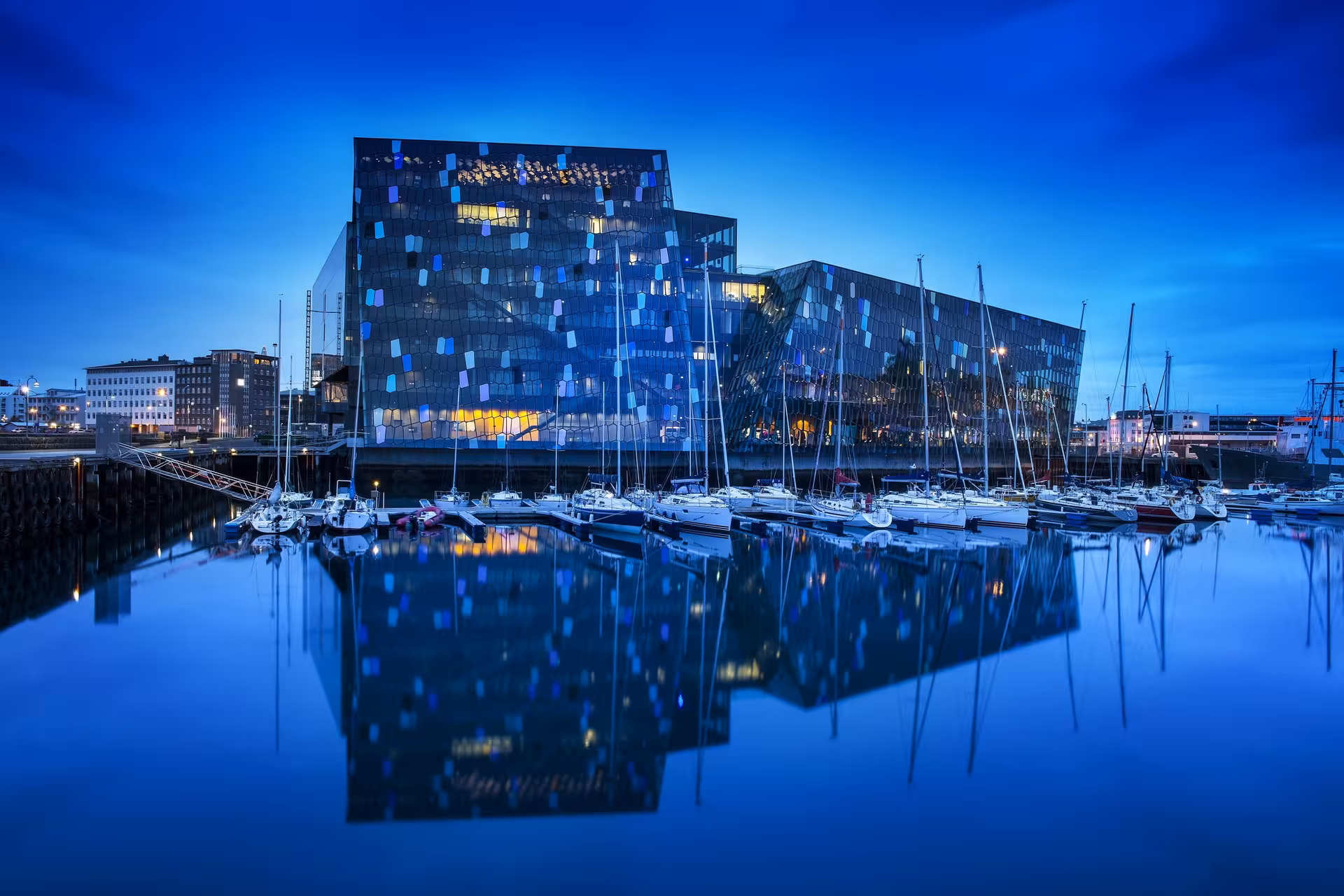 Modern glass building reflects softly in the harbor at twilight, featuring yachts in Iceland's vibrant marina.