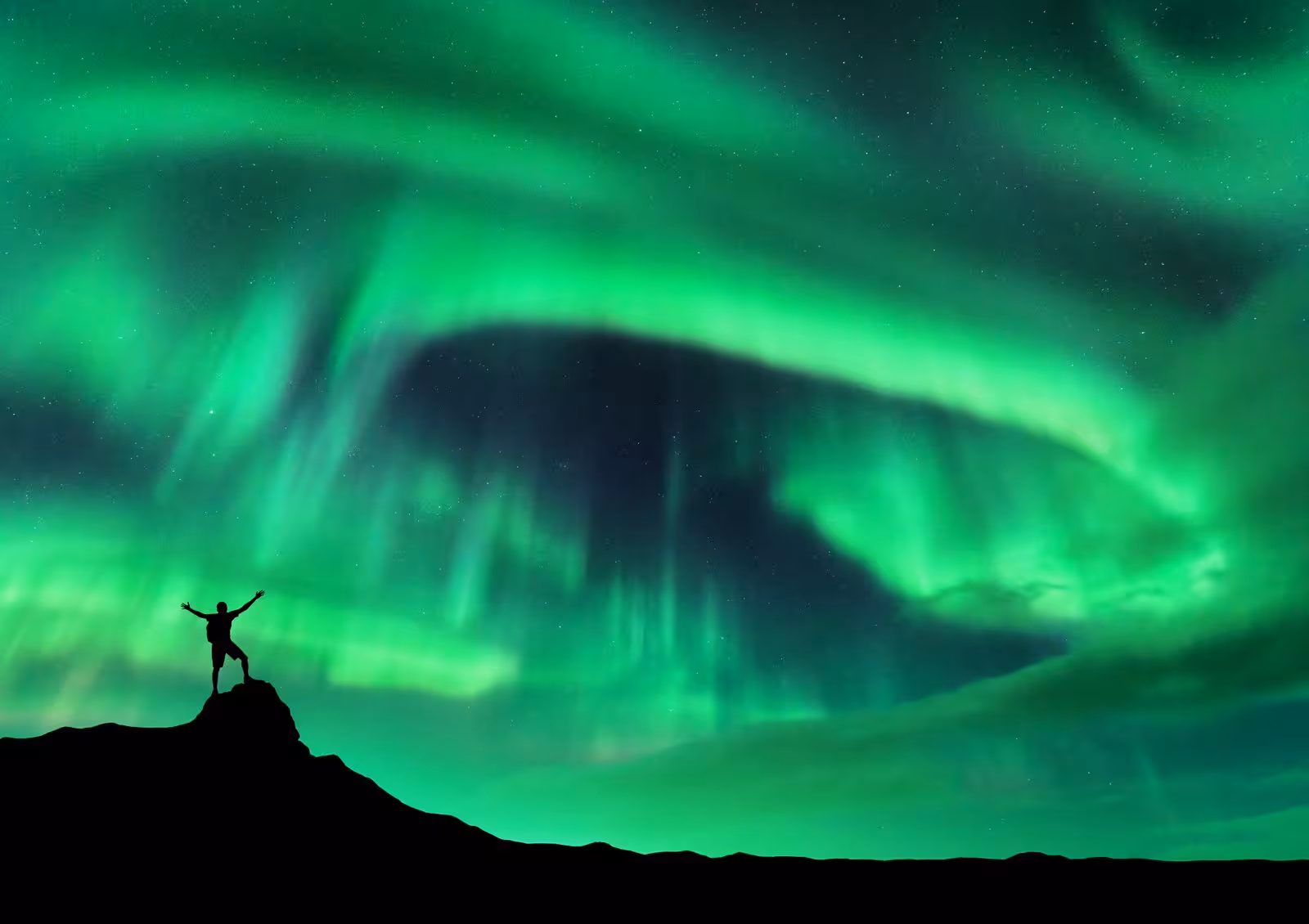 Traveler silhouetted against Iceland's vibrant Northern Lights under a starry night sky.