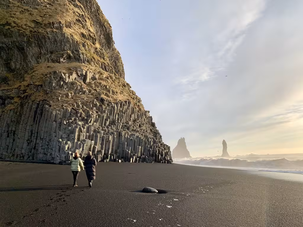 Two women walking along Reynisfjara's black sand beach with stunning basalt columns and sea stacks in Iceland.