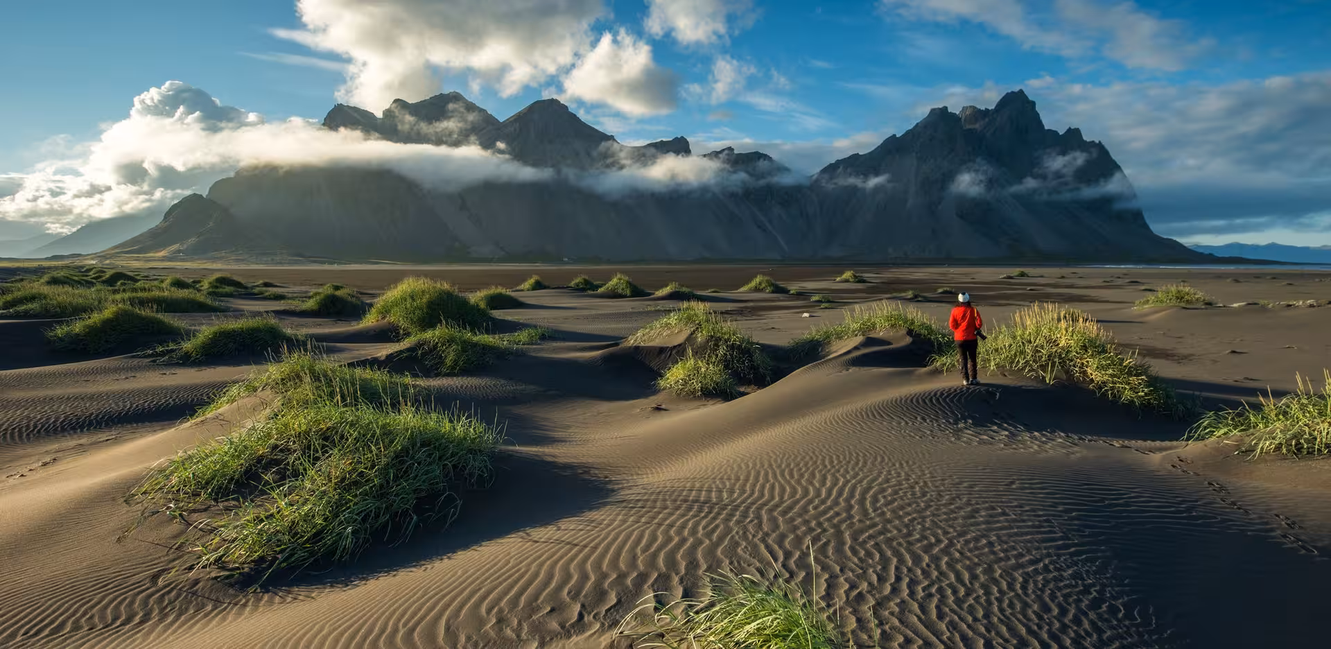 Person in red coat exploring the black sand dunes with Vestrahorn mountain backdrop in Iceland.