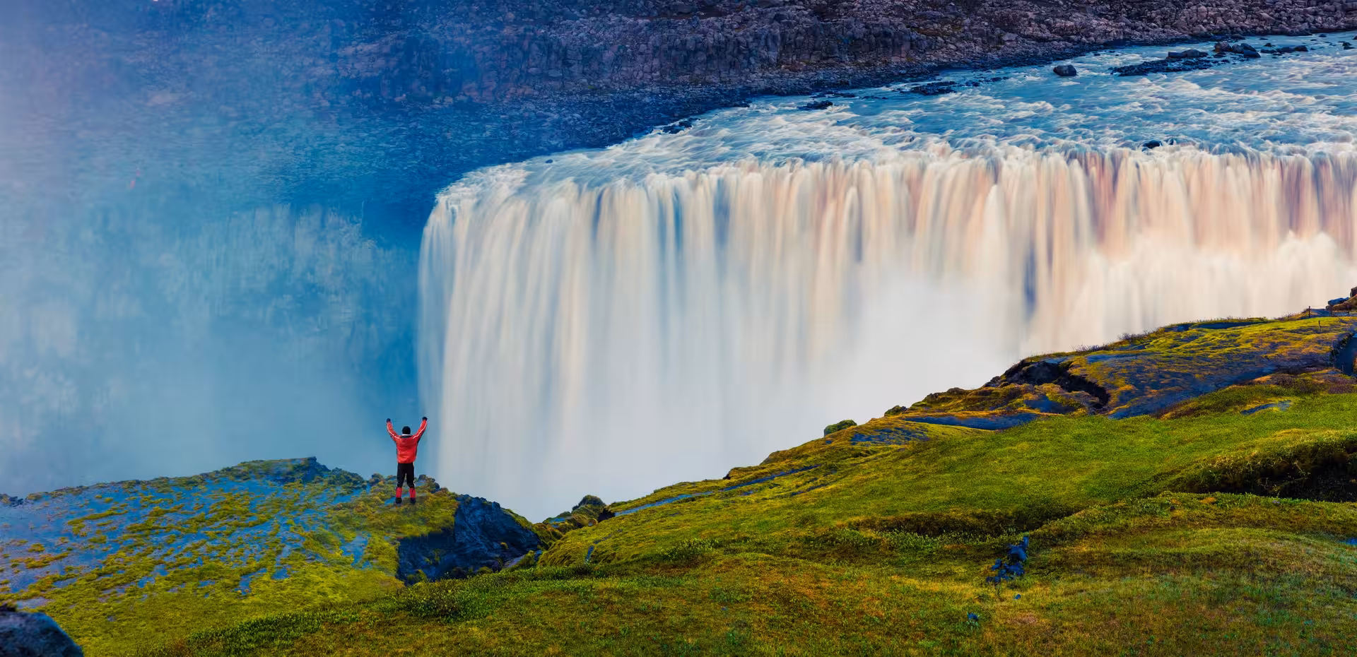 Traveler in red jacket standing near majestic Icelandic waterfall on 10-day self-drive road trip adventure.