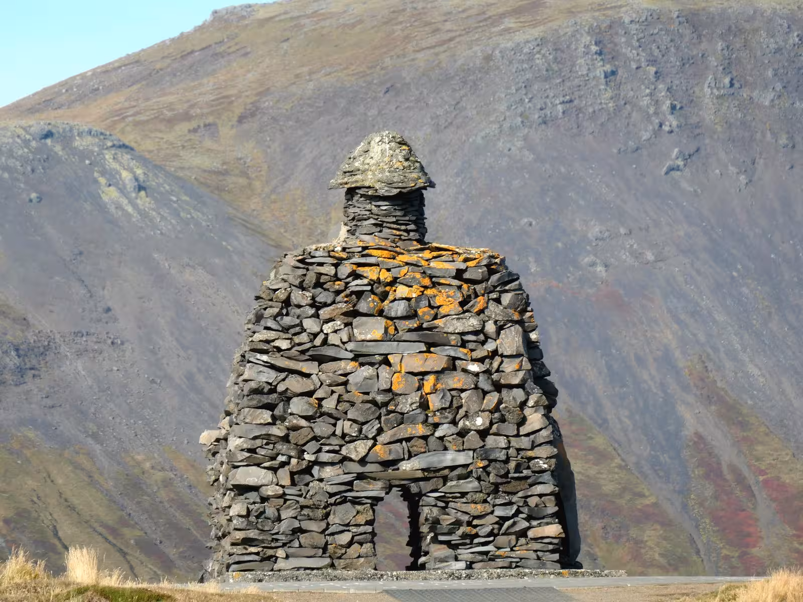 Stone monument against rugged Icelandic mountains, showcasing cultural heritage on a scenic tour.
