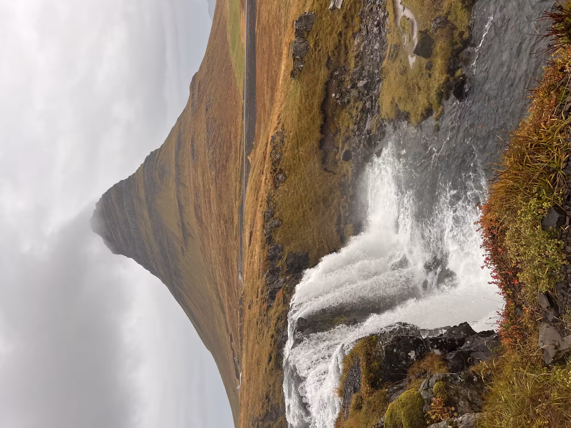 A stunning waterfall cascading beside the iconic Kirkjufell mountain under a cloudy sky in Iceland.