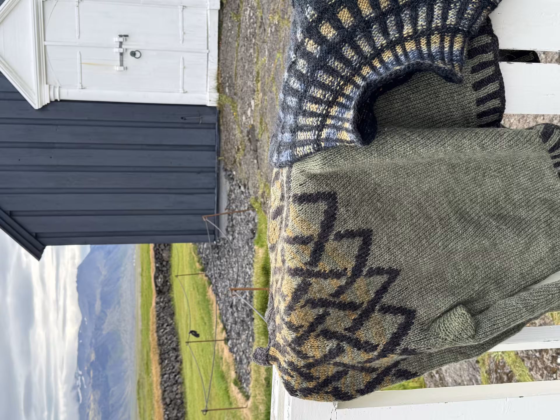 Hand-knitted Icelandic sweaters on a rustic fence with scenic winter landscape, perfect for the Iceland Winter Knitting Tour.
