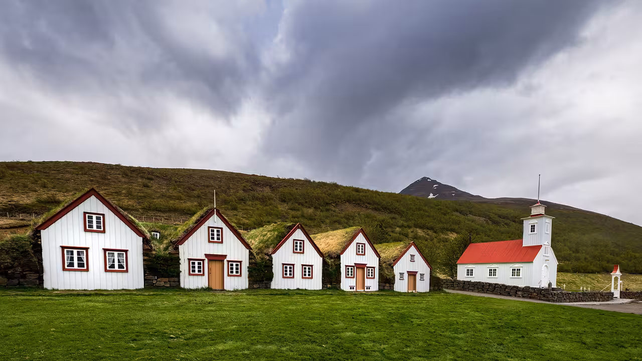 Traditional Icelandic turf houses and church under dramatic skies, part of the Akureyri 4x4 tour experience.
