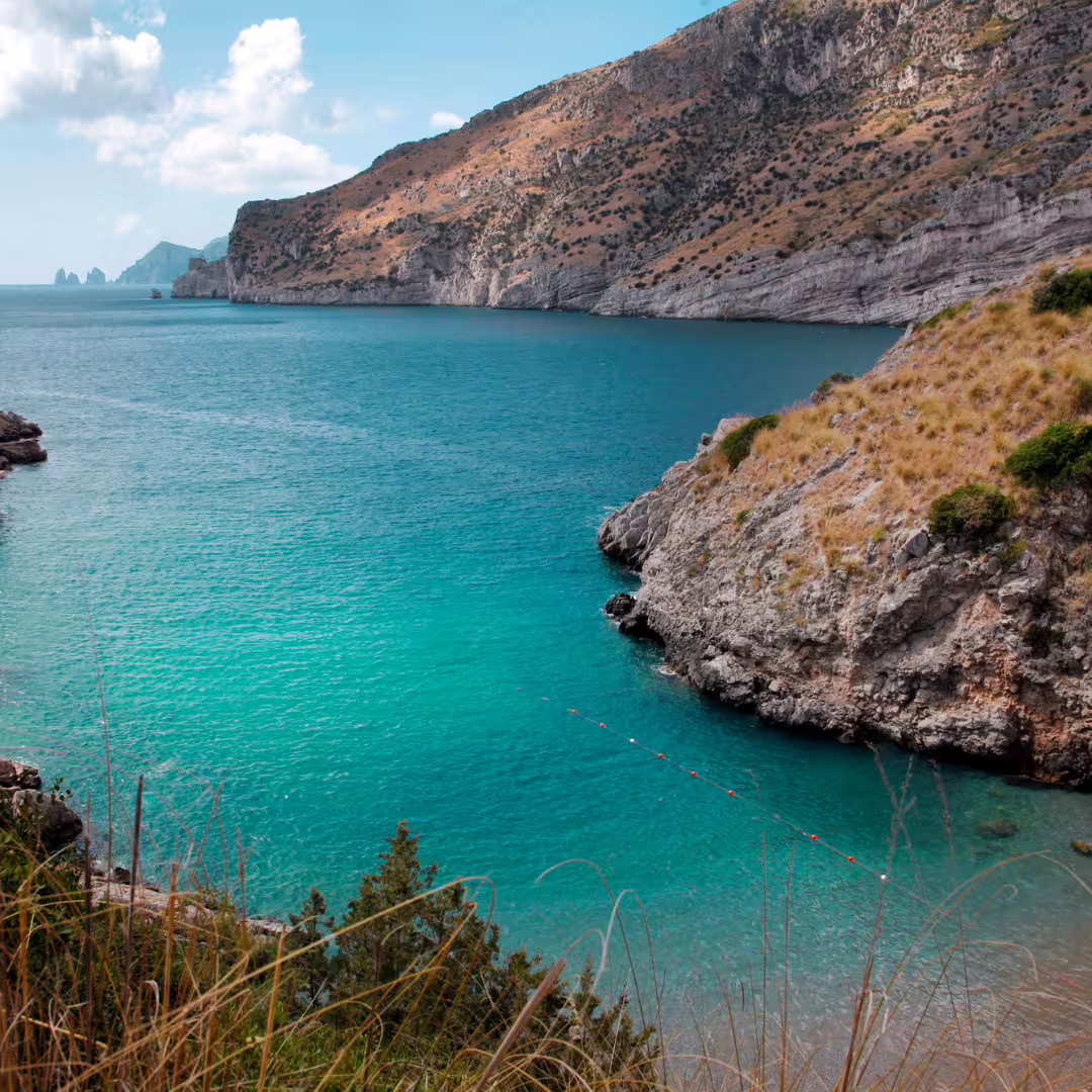 Crystal-clear turquoise cove of Ieranto Bay framed by rocky cliffs on Punta Campanella trekking weekend from Sorrento