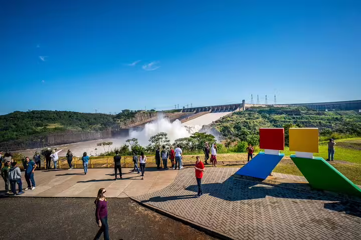 Tourists admire the stunning view of Itaipu Dam amidst lush greenery on a clear day during the Iguazu Falls tour.