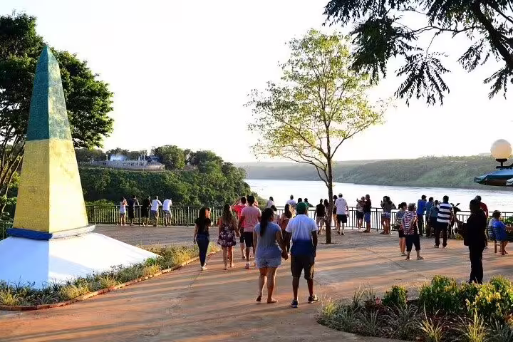 Tourists enjoying the scenic Three Borders Landmark, overlooking the confluence of Iguazu and Paraná rivers at sunset.